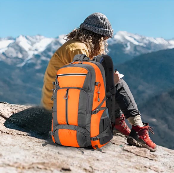 Sac à dos orange posé côté jeune alpiniste assise au sommet montagne